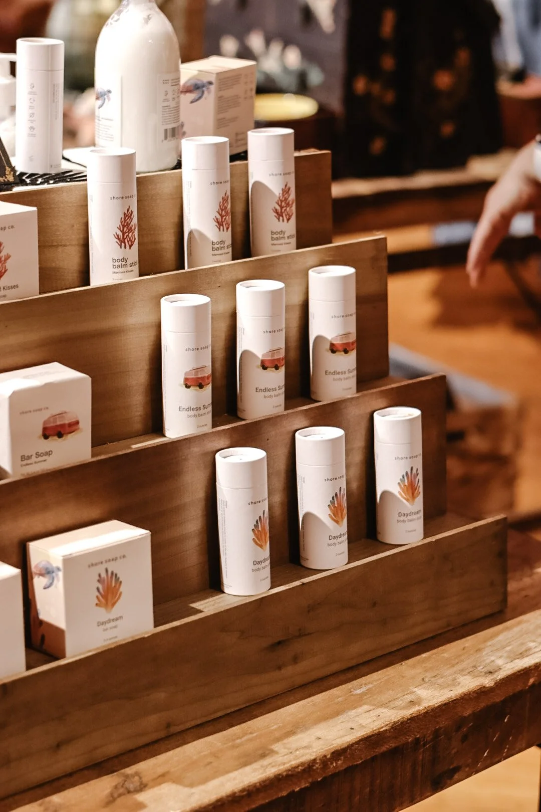 Display shelf with various skincare or body care products in white containers with minimalistic labels, wood stand on a wooden table.