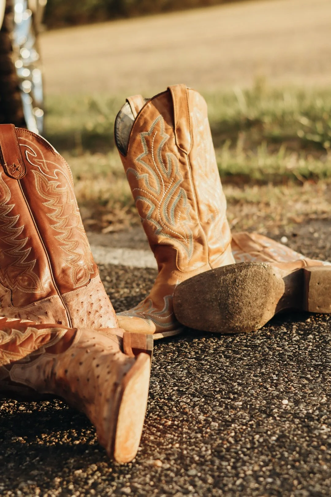 A pair of orange cowboy boots with embroidered designs and worn soles resting on the ground outdoors.