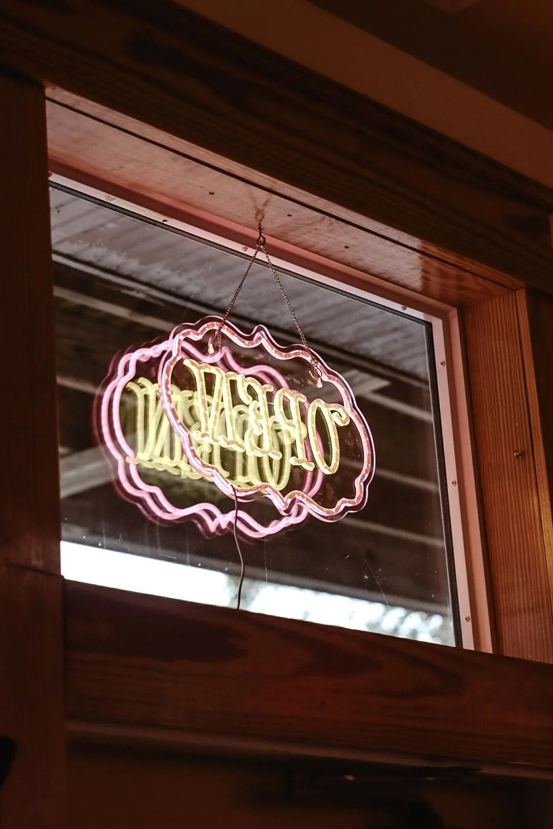 Neon sign reading 'OPEN' hanging inside a window with wooden framing.