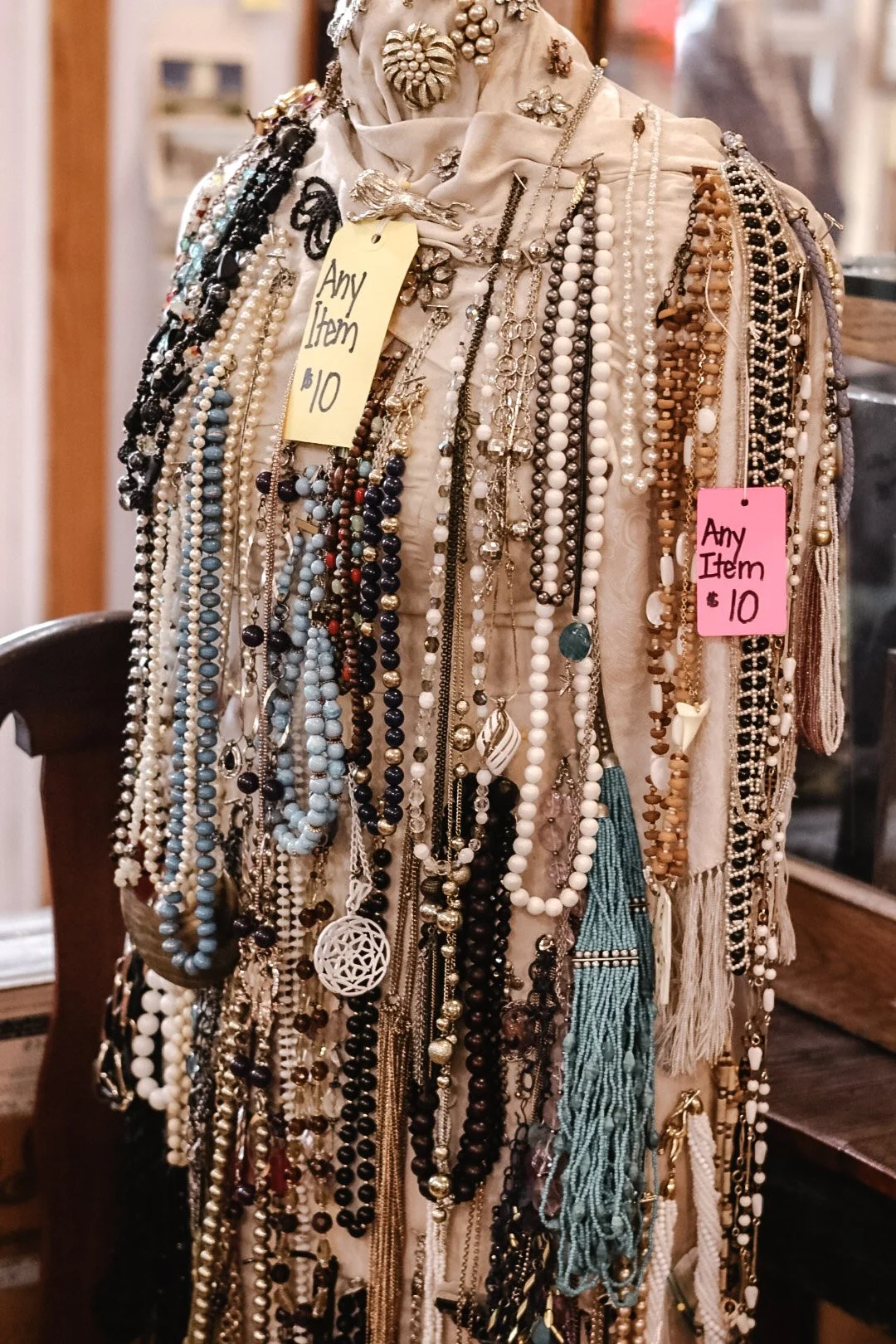 A display of assorted necklaces hanging on a stand with yellow and pink price tags, indicating any item for $10.