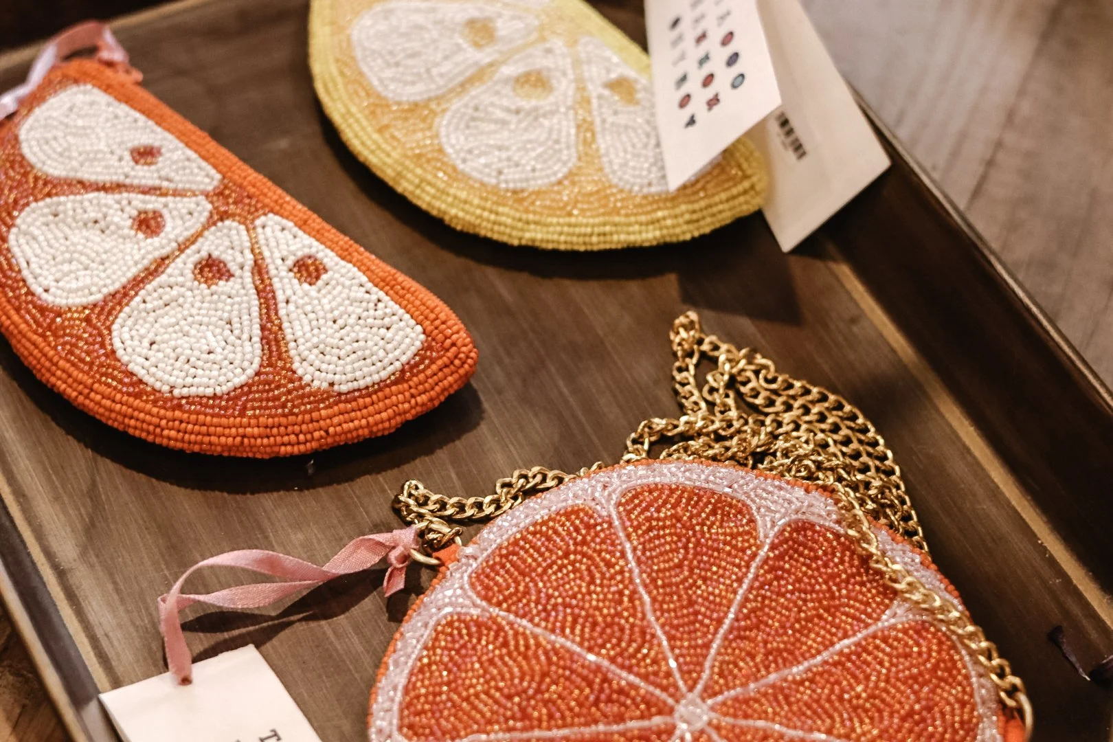 Decorative orange and white beaded clutch purses with gold chains, displayed on a wooden surface.