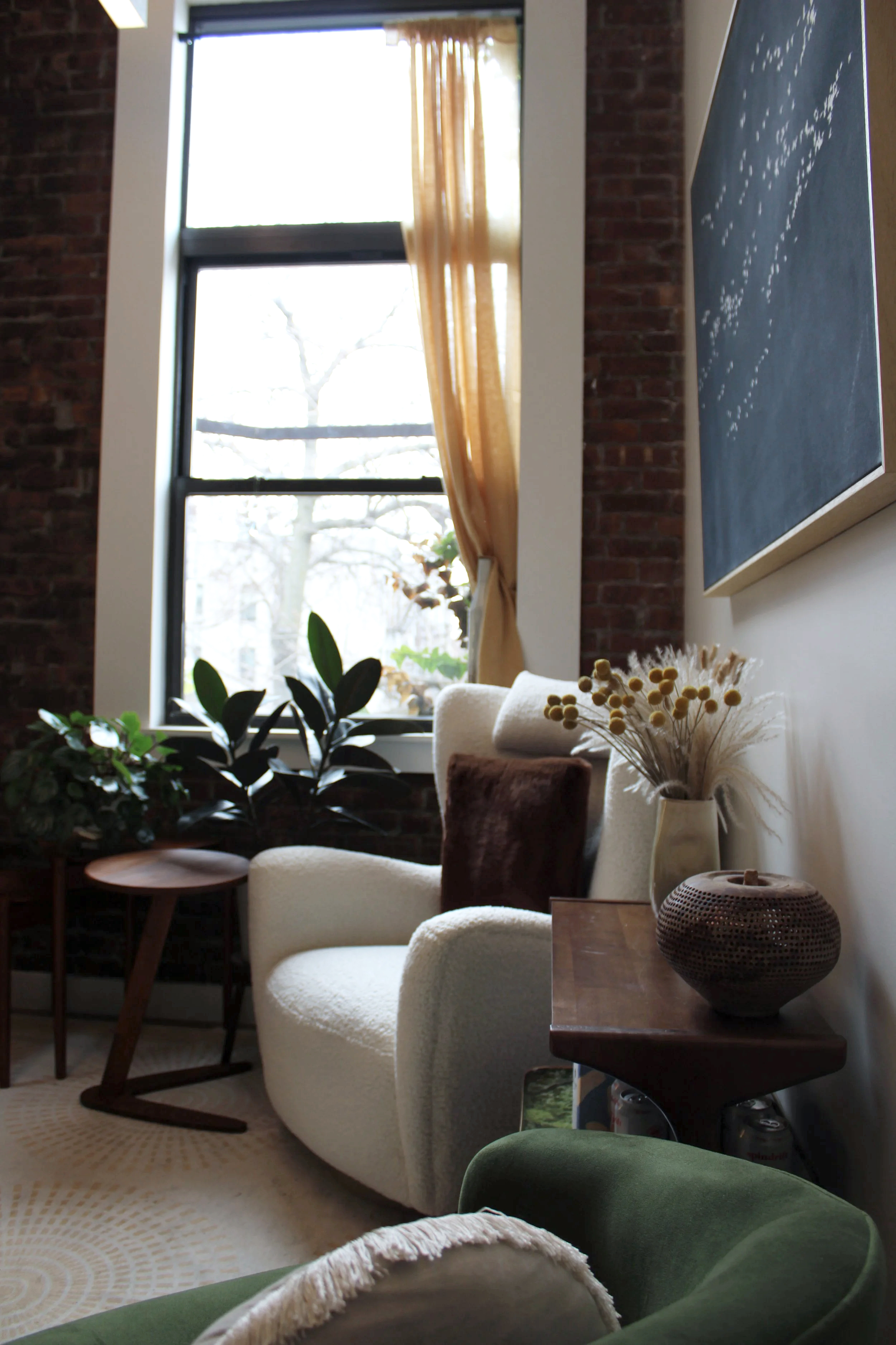 Photo of the Gotham Well Being consultation office: a creme-colored cushioned chair with a brown cushion, next to a window that has a gold-ish toned curtain pulled back.