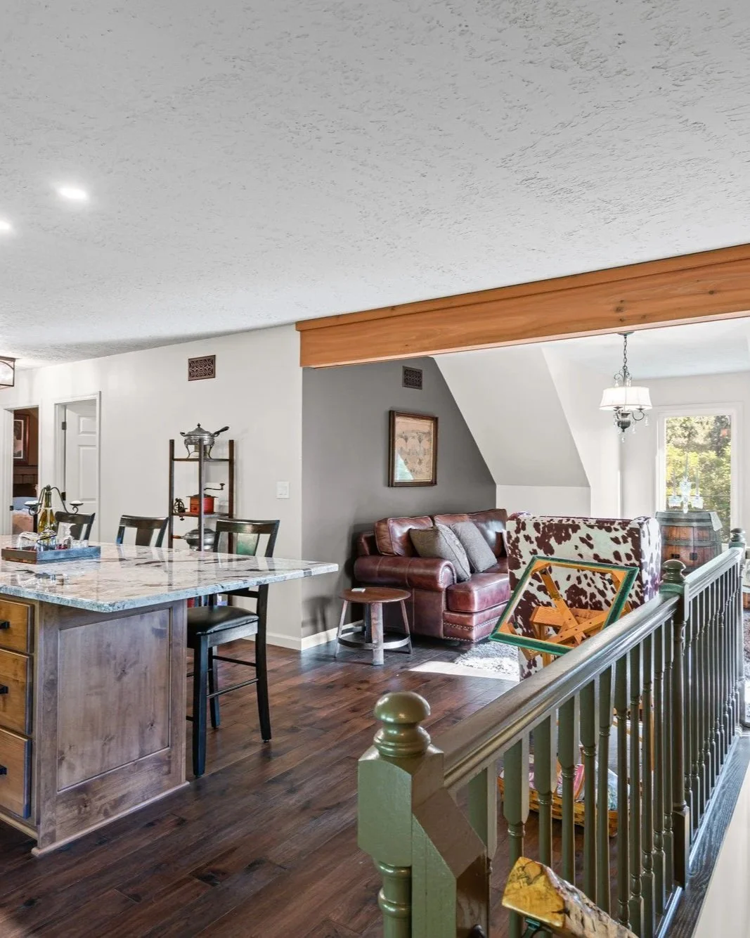 Living room with a granite kitchen island, leather sofa, cowhide armchair, wood accents, and chandelier