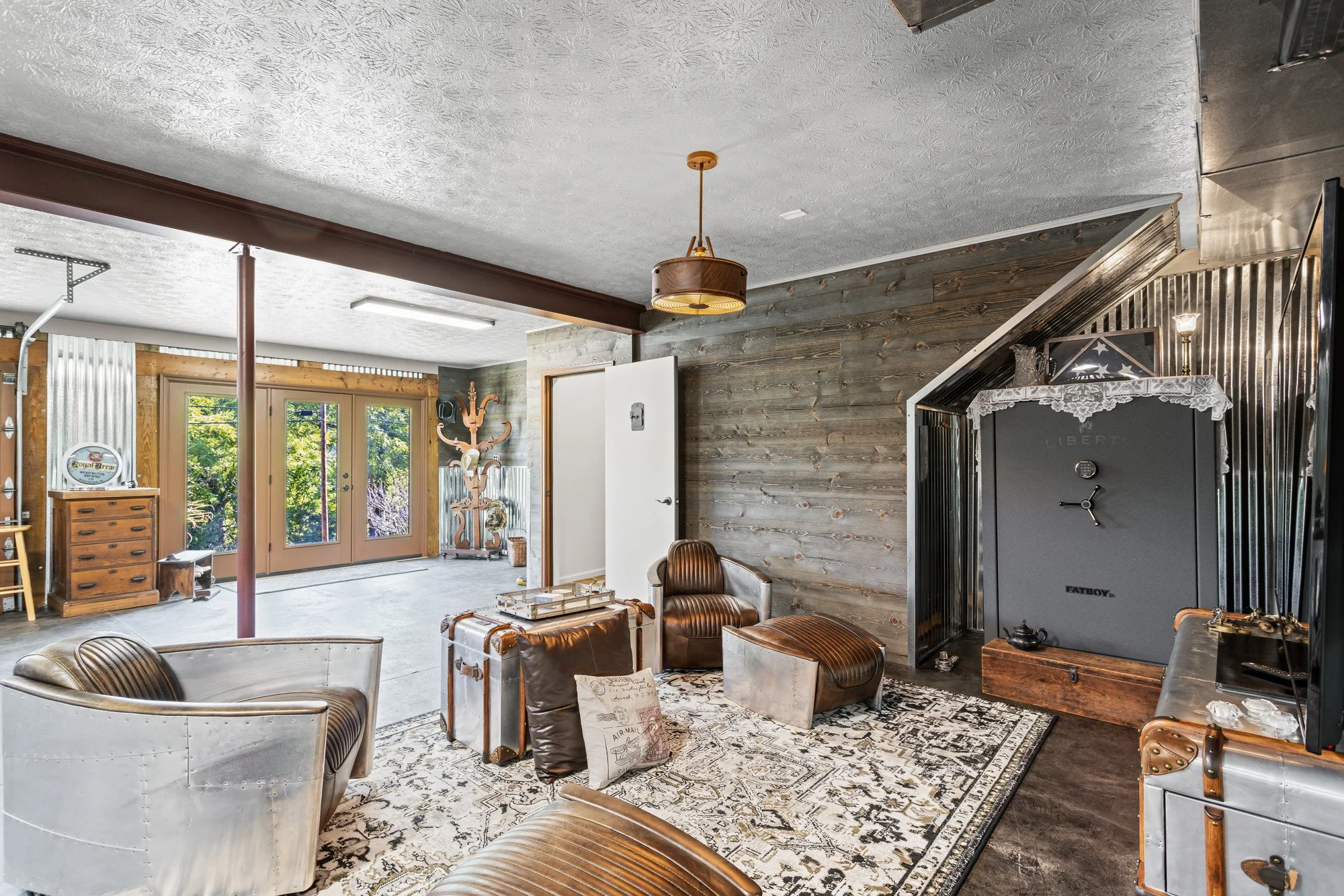 Living room with leather armchairs, a vintage-style rug, a black gun safe, and rustic wood accents, with a view of outdoors through glass doors.