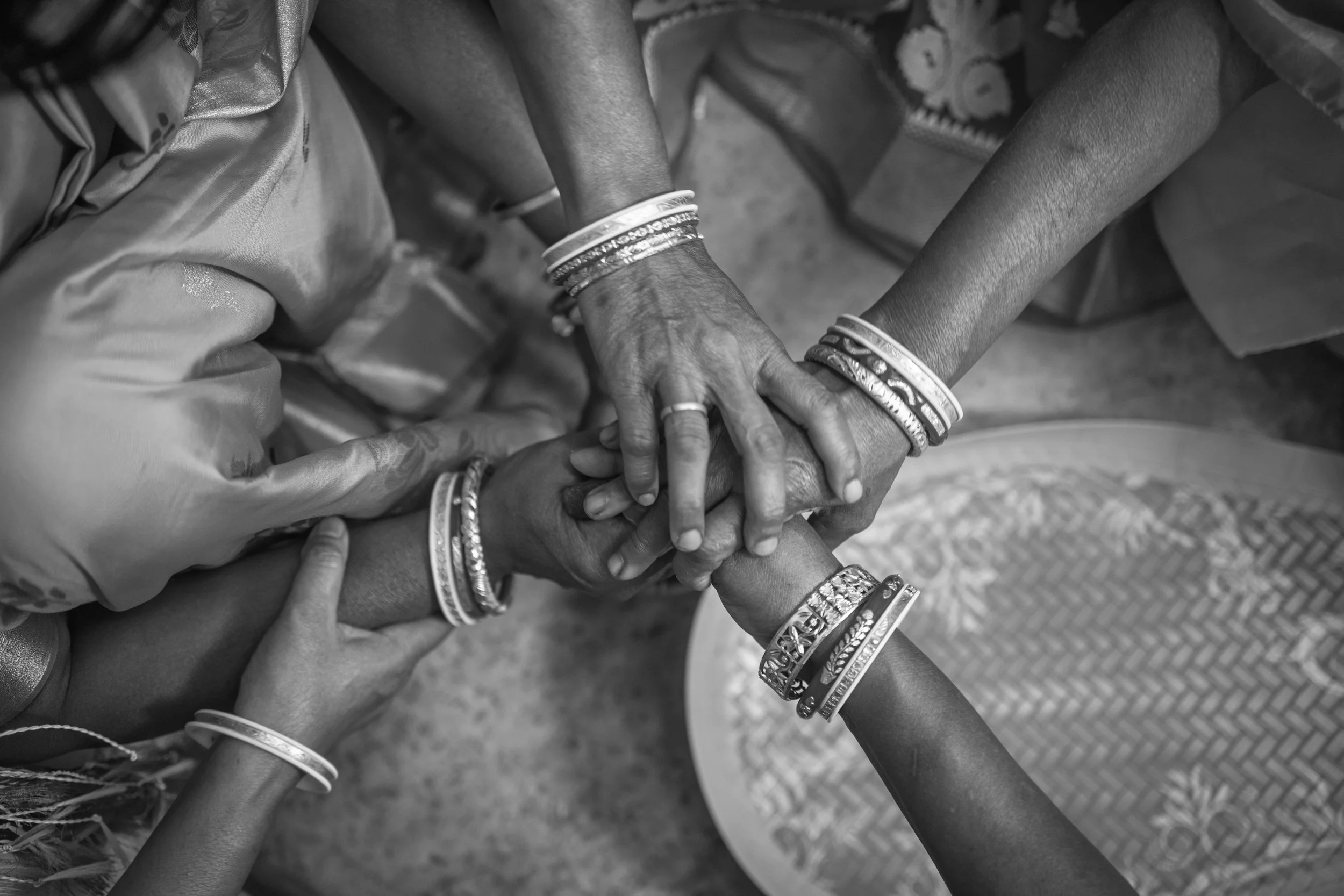 Black and white photo of multiple hands stacked together, with various wristbands and bracelets visible.