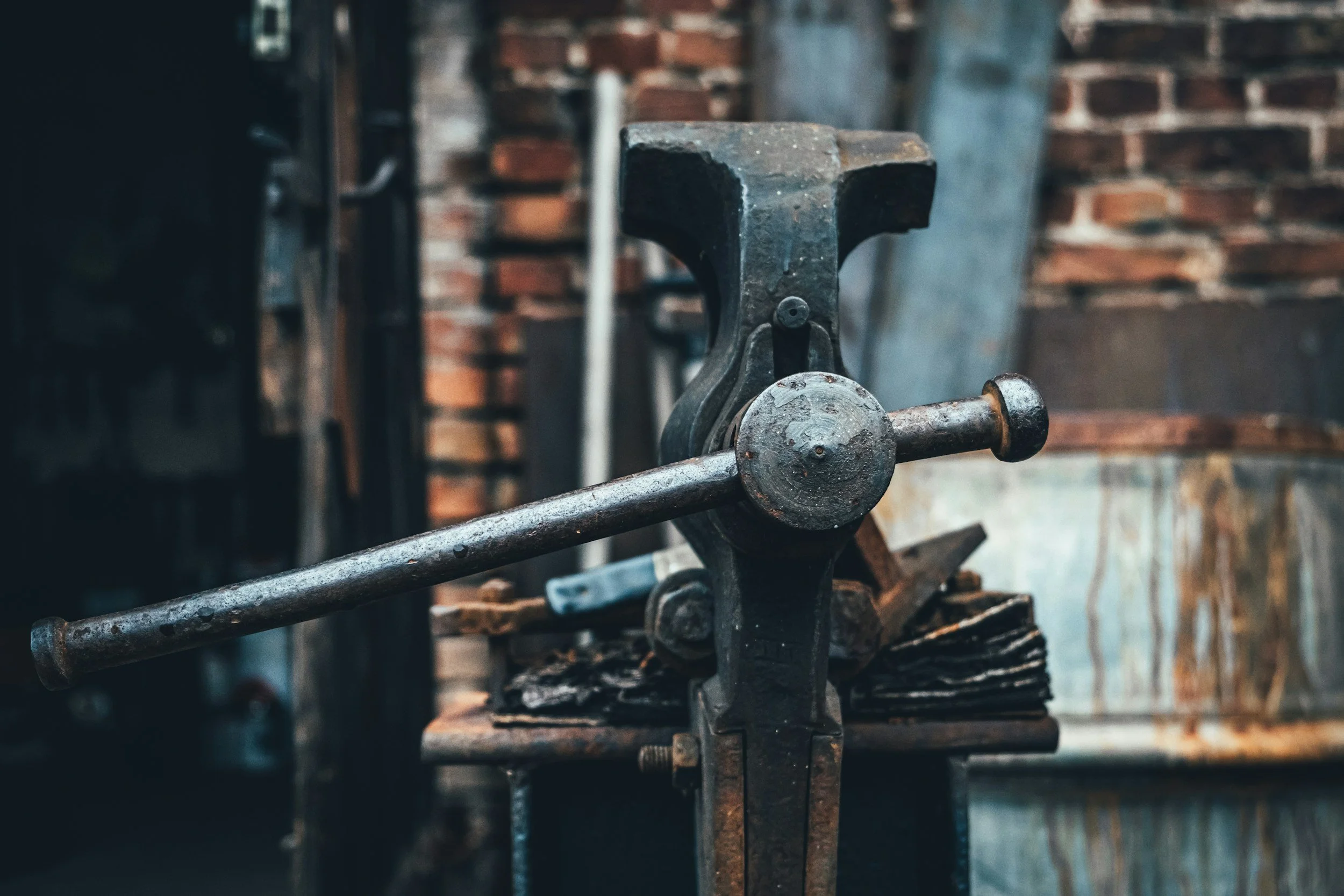 Close-up of a vintage blacksmithing hammer held in place on an anvil in a workshop with brick walls.