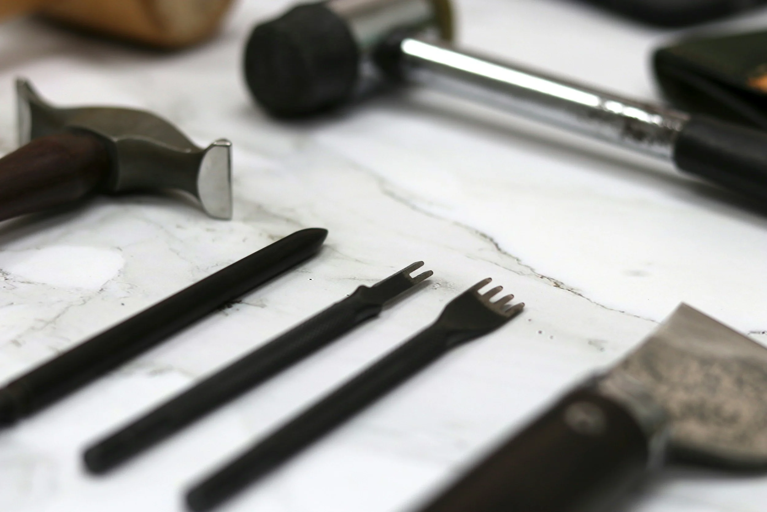 A close-up photo of various black hair styling tools, including combs and a hairbrush, on a white marble surface.