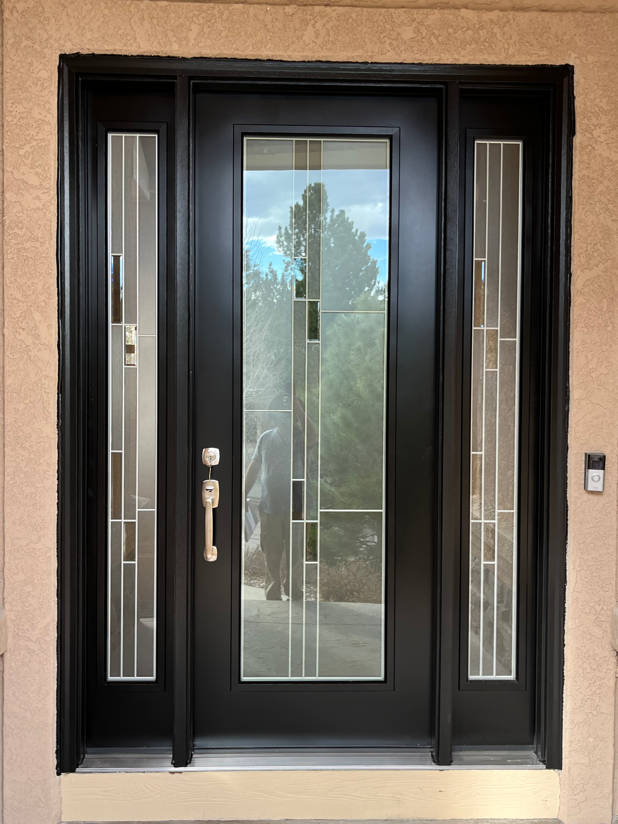 A black framed glass front door with decorative glass panels on either side, set in a peach textured wall.