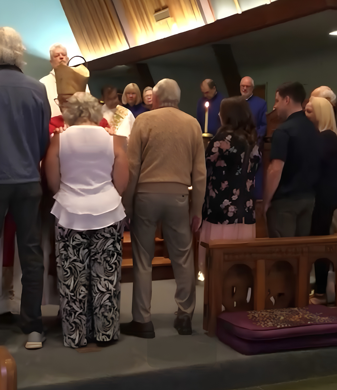 People gathered around a baptismal font during a church baptism ceremony, with a priest performing the ritual.