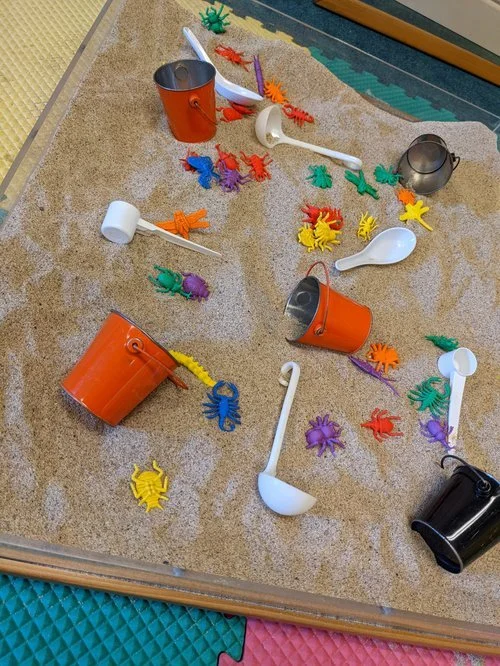 Colorful plastic insects and buckets spilled on a carpeted indoor play area.