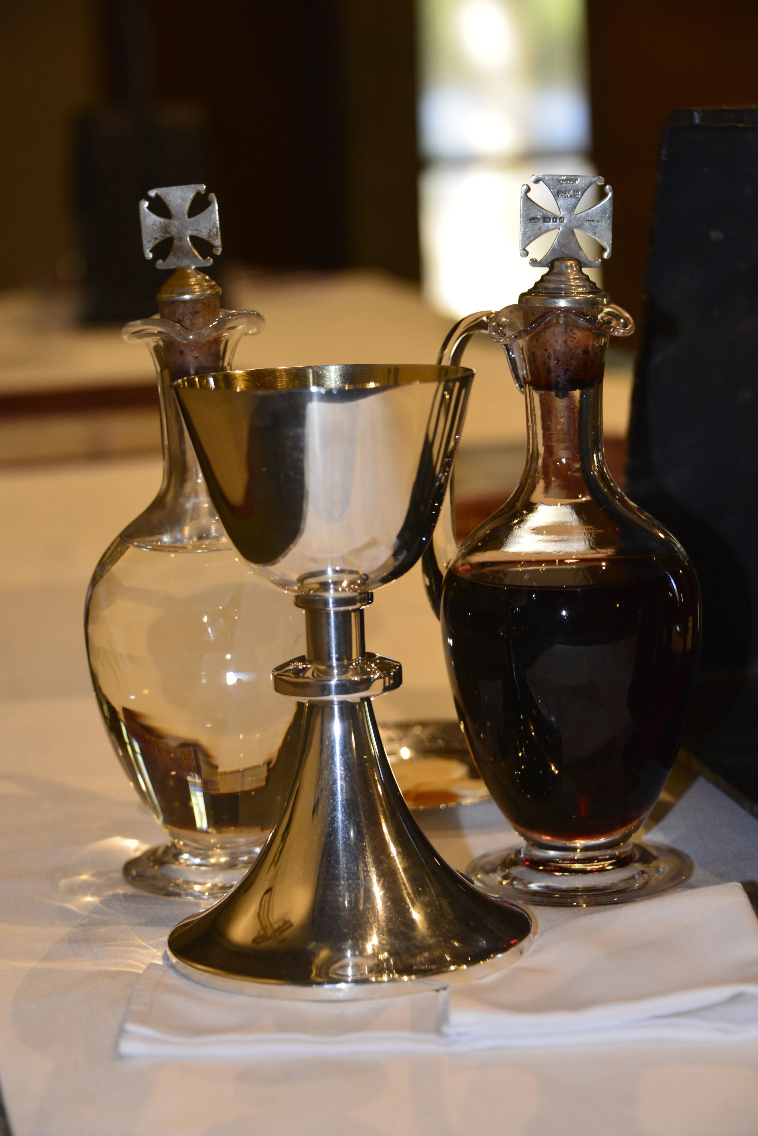 Three glass bottles with metal condiment toppers, two cutlery holders, and a shiny gold-colored standing holder on a white tablecloth.