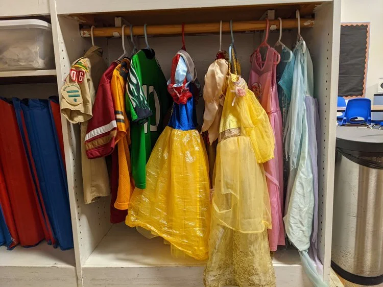 Wardrobe with various children's costumes, including princess dresses and superhero outfits.