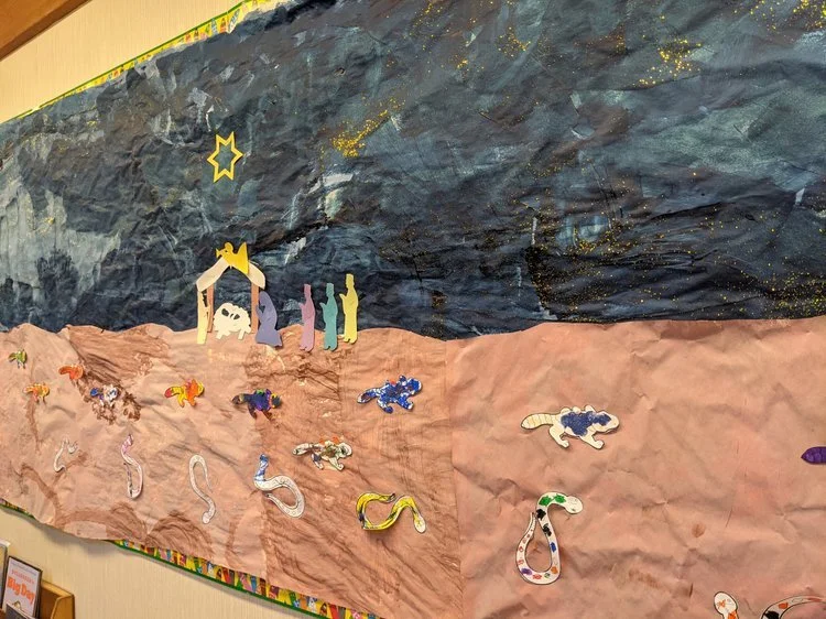 A classroom bulletin board decorated with a nativity scene and a collage of sea creatures on crumpled paper, representing a manger scene and the ocean.