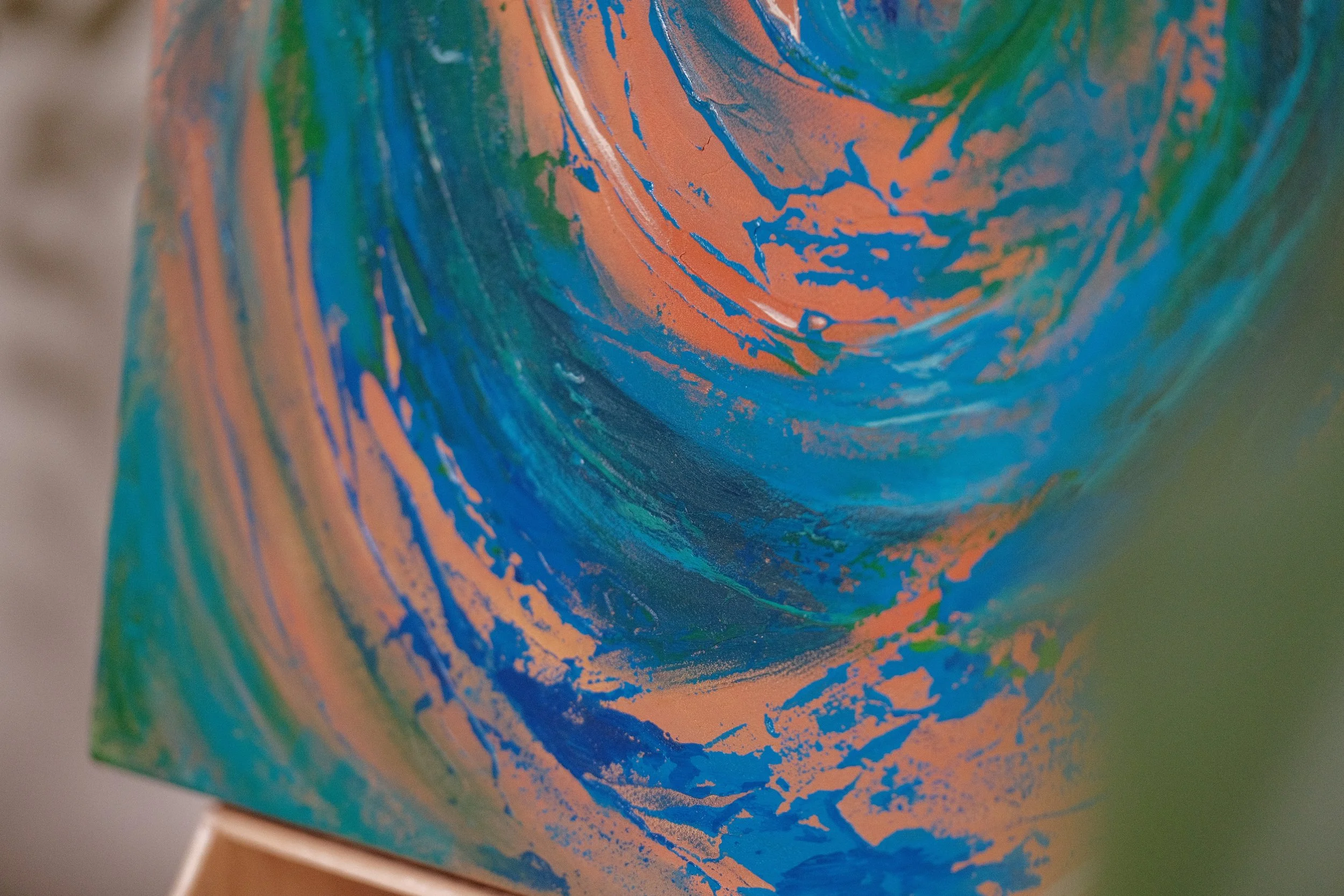 Close-up of a colorful abstract painting with swirls of blue, green, and orange.