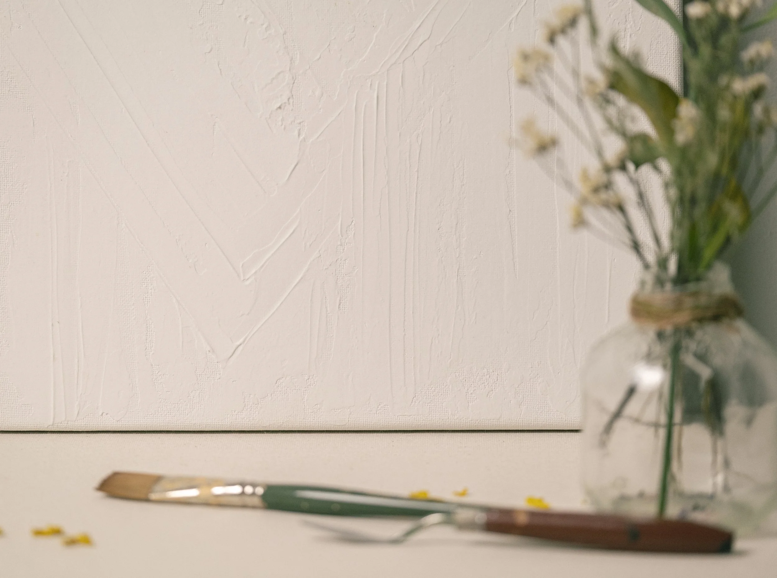 A blank textured white canvas with a painter's brush lying at the bottom and a blurred branch of flowers and leaves on the right side.