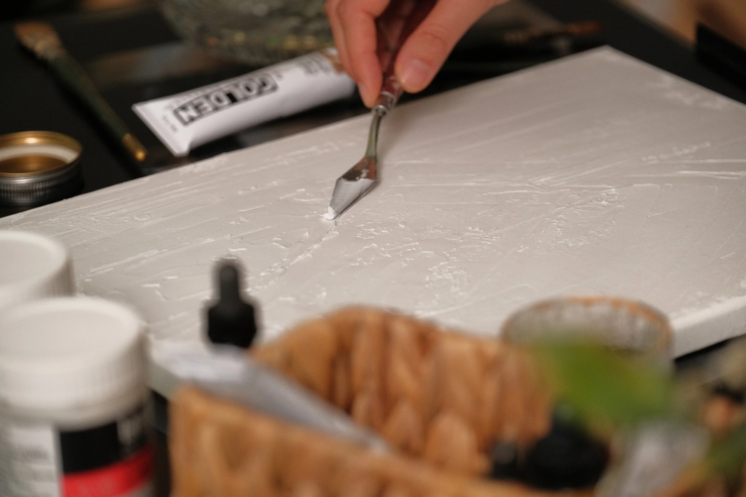 Close-up of a person using a tool to cut into a white surface, with a tube of adhesive and other items nearby.
