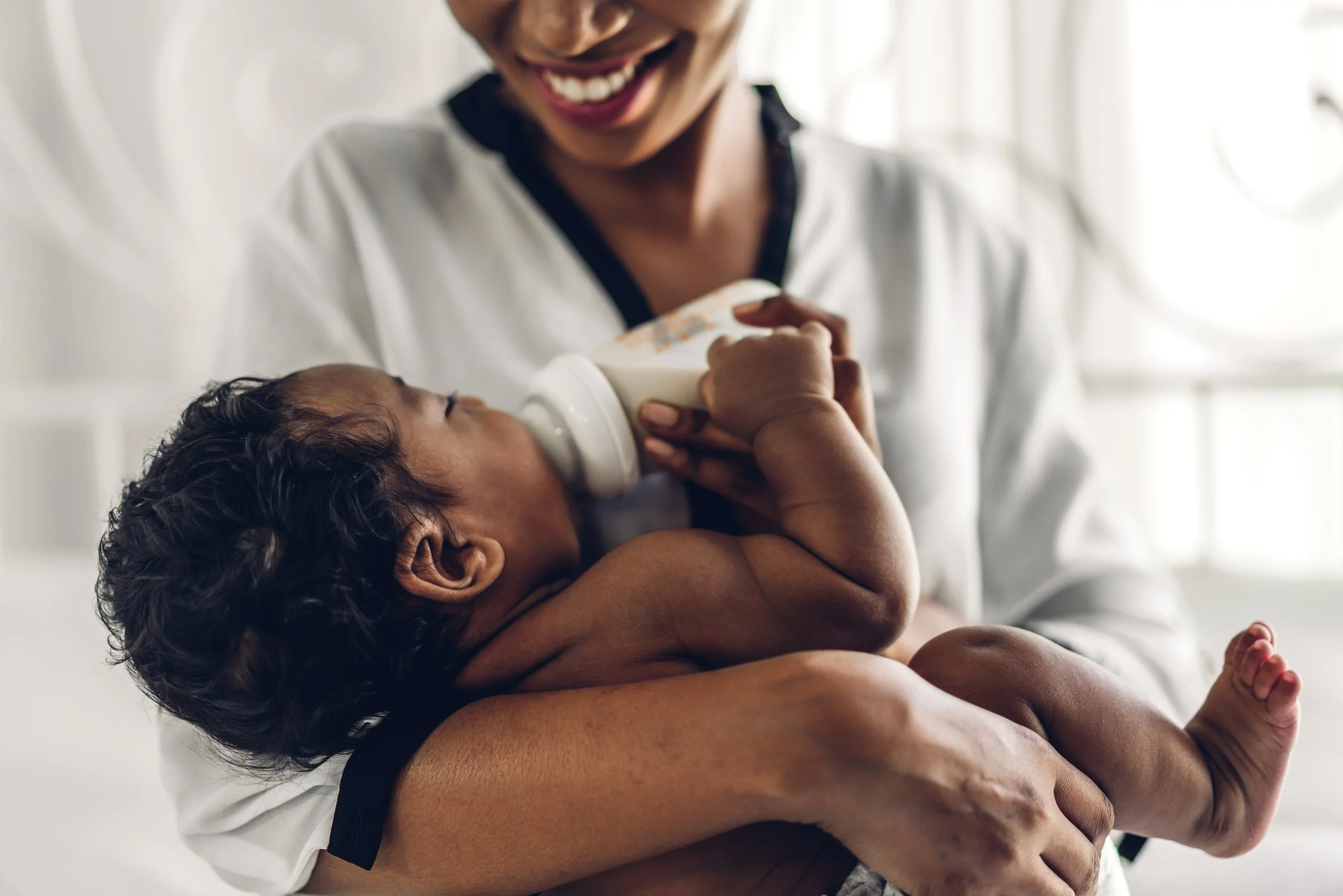 A woman in a white shirt smiling while holding a baby who is working on bottle feeding during feeding therapy for infants in Athens, GA.