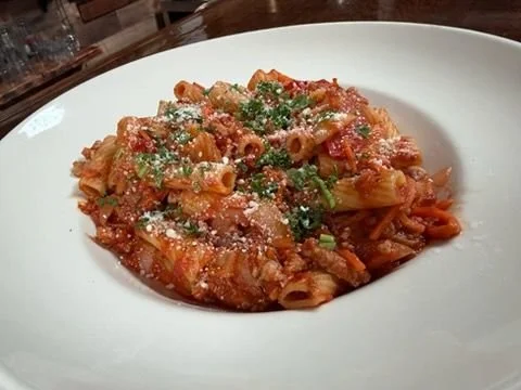 Plate of pasta with tomato sauce, garnished with grated cheese and chopped herbs.