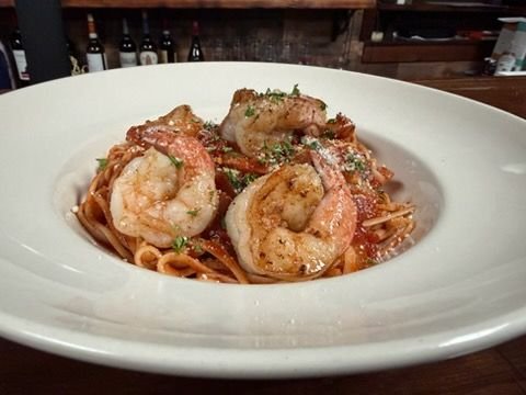 Shrimp pasta in a white bowl garnished with herbs, served in a restaurant setting.
