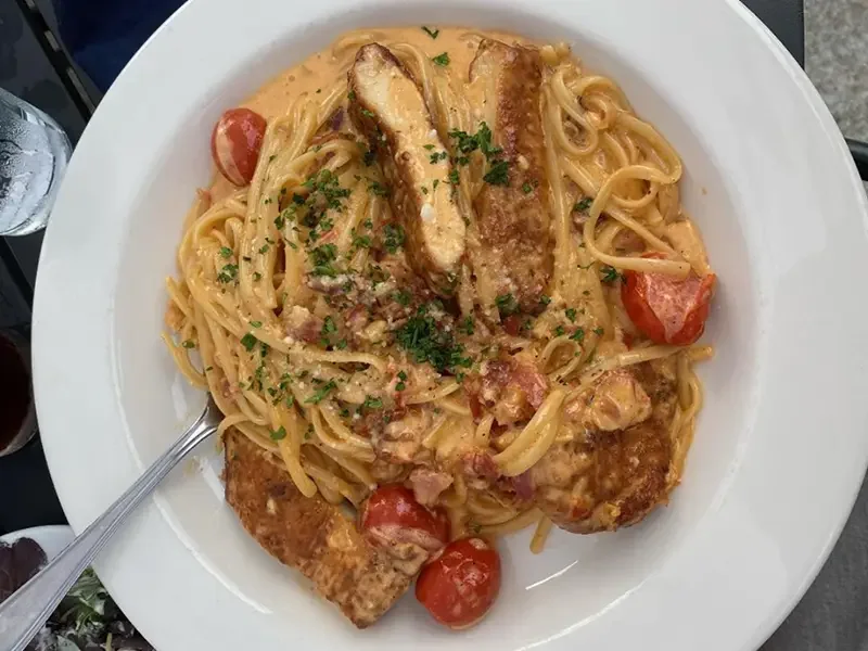 Plate of creamy pasta with cherry tomatoes, grilled chicken, and chopped parsley.
