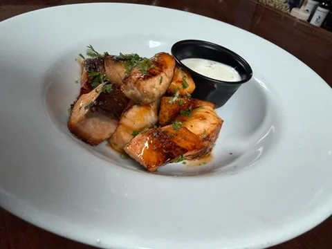 Plate of cooked shrimp with seasoning and herbs, served with a cup of creamy dipping sauce.