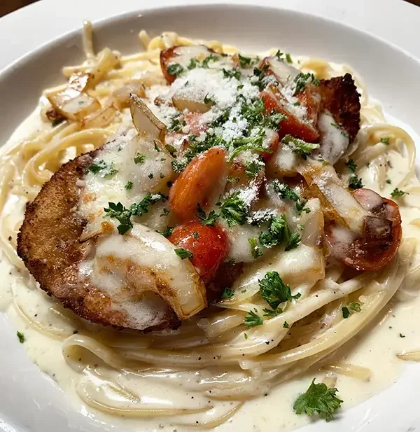 Spaghetti topped with grilled chicken, cherry tomatoes, onions, parsley, and grated cheese in a creamy white sauce.