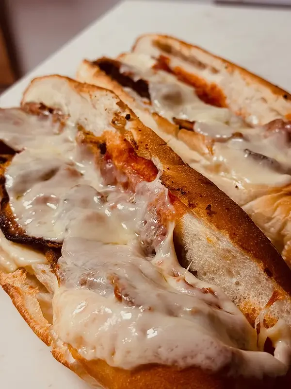 Close-up of a sliced Italian hoagie sandwich with melted cheese, roasted mushrooms, and deli meats on a white bun.