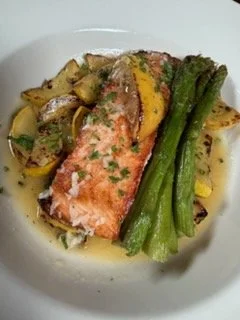 A plated dish featuring a cooked salmon fillet with a lemon wedge, served with asparagus spears and sautéed vegetables.