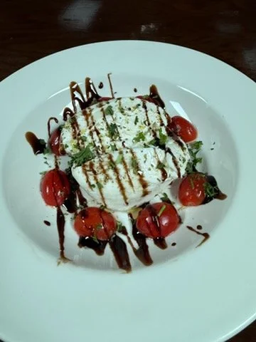 A dessert with two scoops of vanilla ice cream topped with chocolate drizzle, garnished with cherry tomatoes, mint leaves, and drizzled with syrup on a white plate.