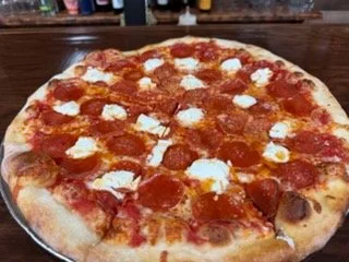 Whole pepperoni and cheese pizza on a black tray.