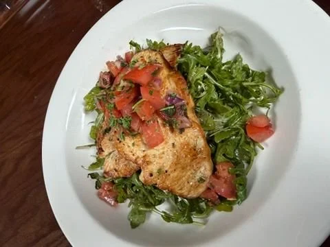 Grilled chicken breast with tomato and lettuce salad on white plate.