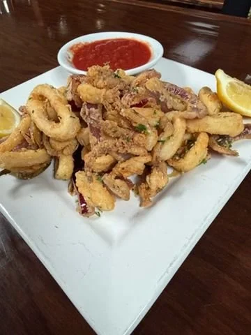 Fried calamari served with a side of marinara sauce and lemon wedges on a white plate