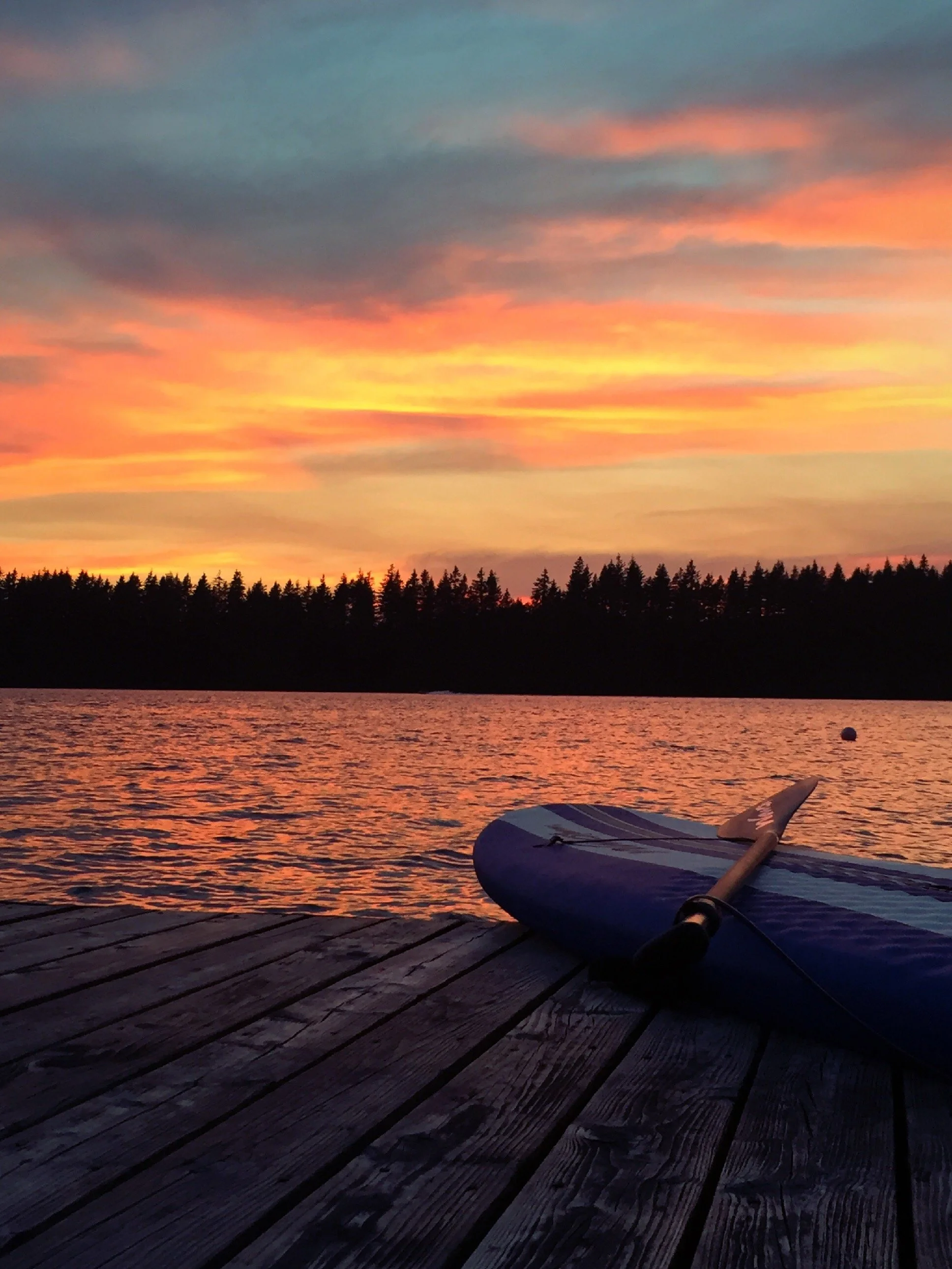 Paddleboard on a dock at a lake with a sunset in the background.