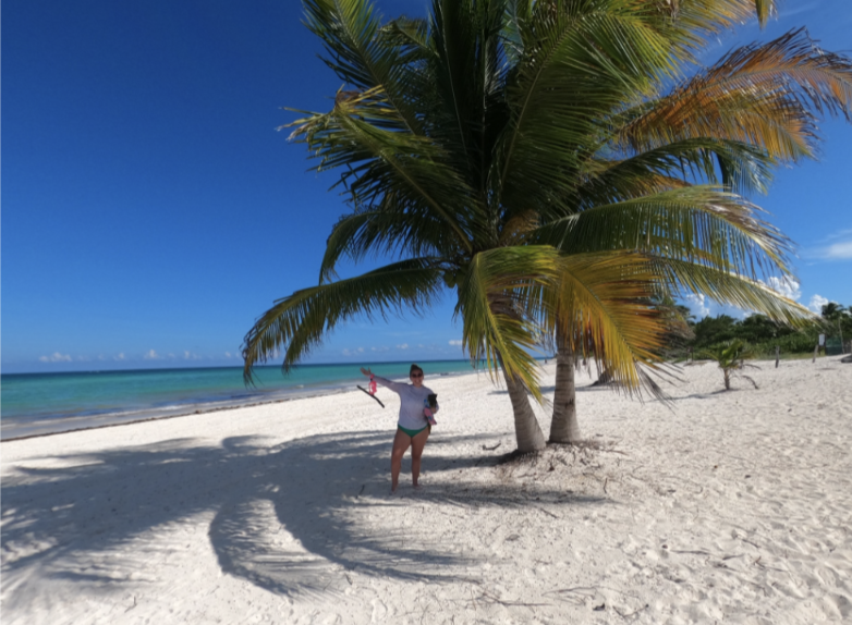 Woman under a palm tree on a beach holding snorkeling gear.