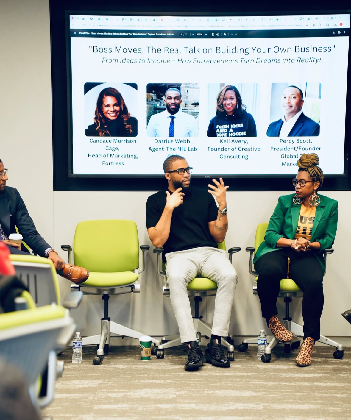 Panel discussion with three people seated in front of a large screen displaying panelist photos and names. The screen title is "Boss Moves: The Real Talk on Building Your Own Business." The panelists include Candace Morrison Cage, Darrius Webb, Keli Avery, and Percy Scott.