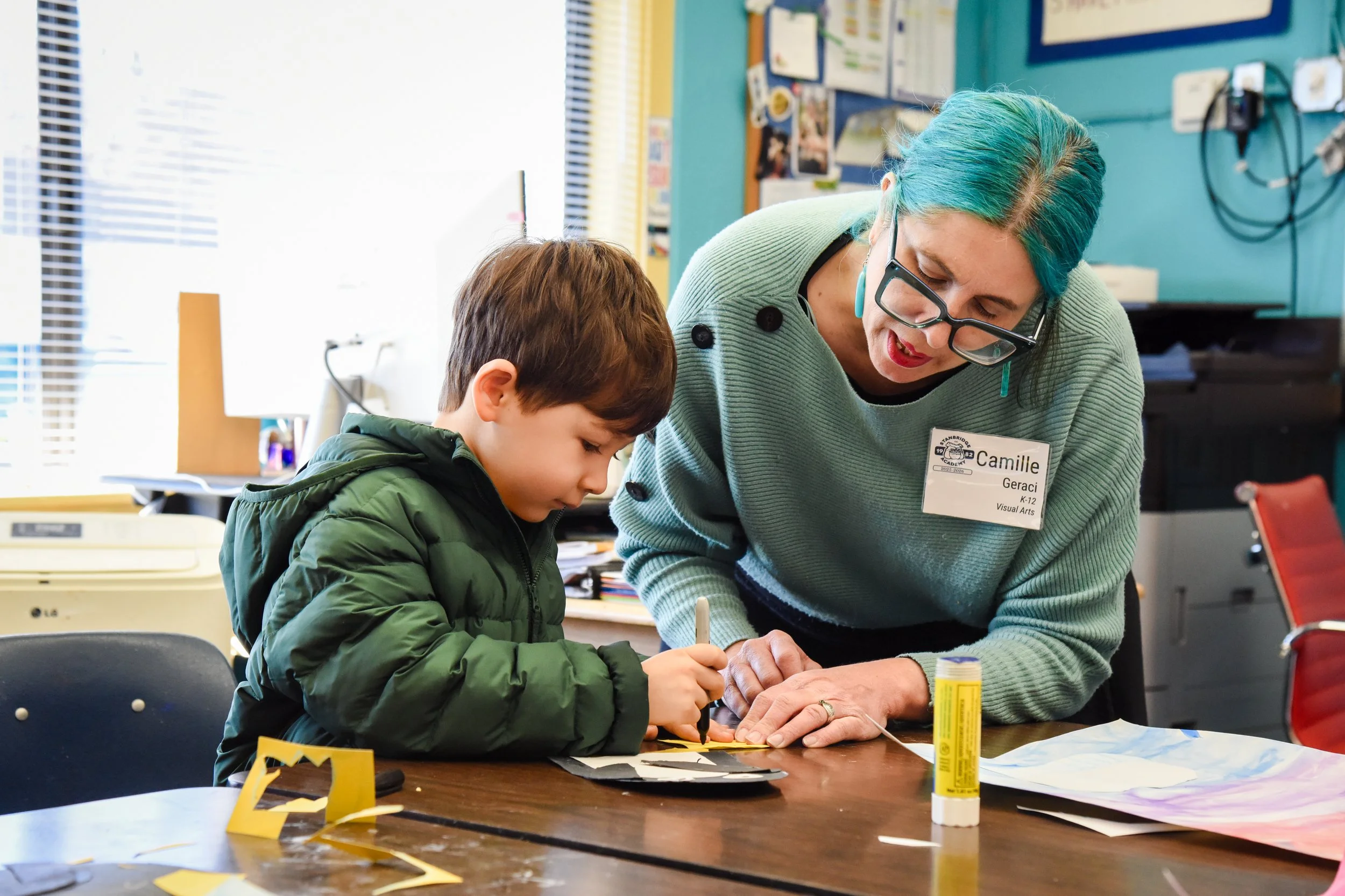 elementary student working on an art project and getting support from the art teacher