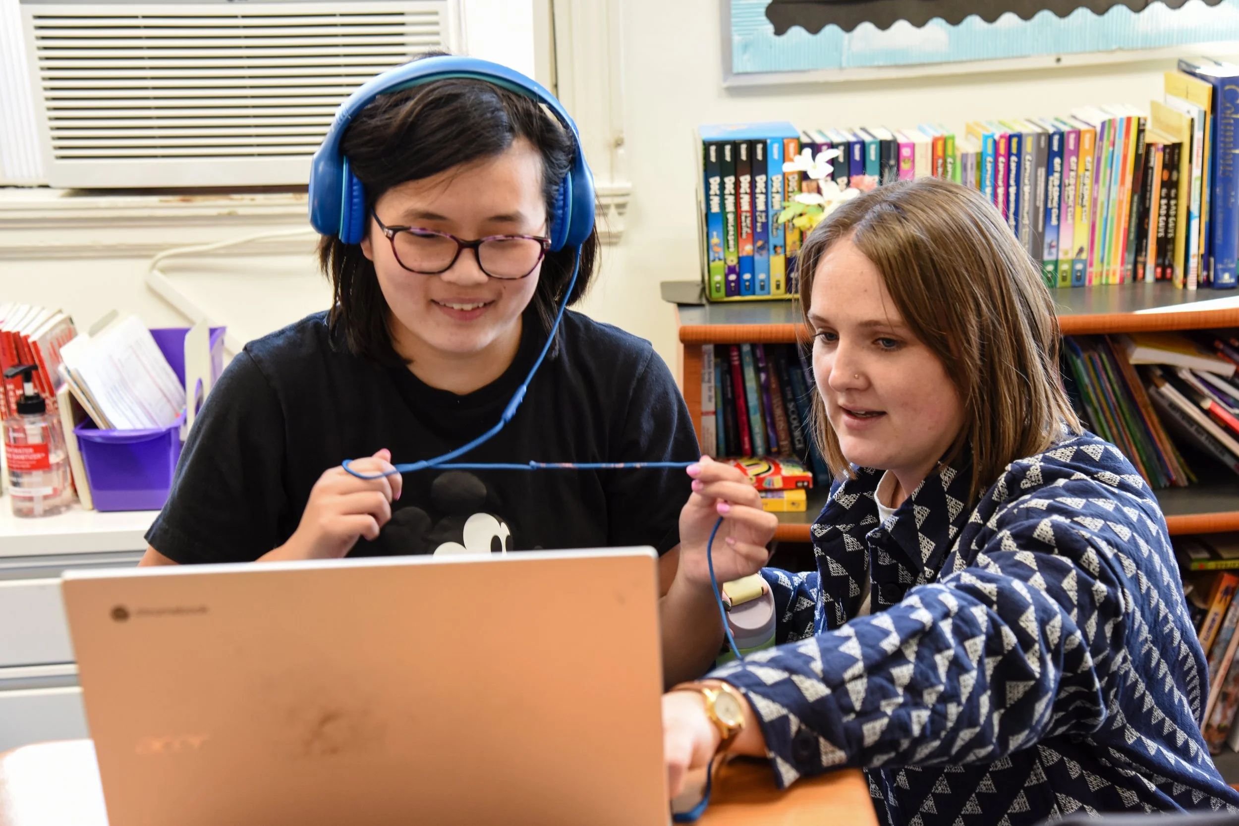 student with headphones on laptop getting support from a teacher