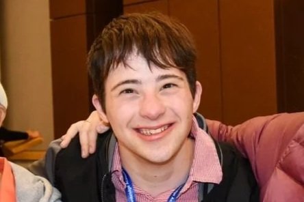 Smiling young man with short brown hair posing with someone at an indoor event.