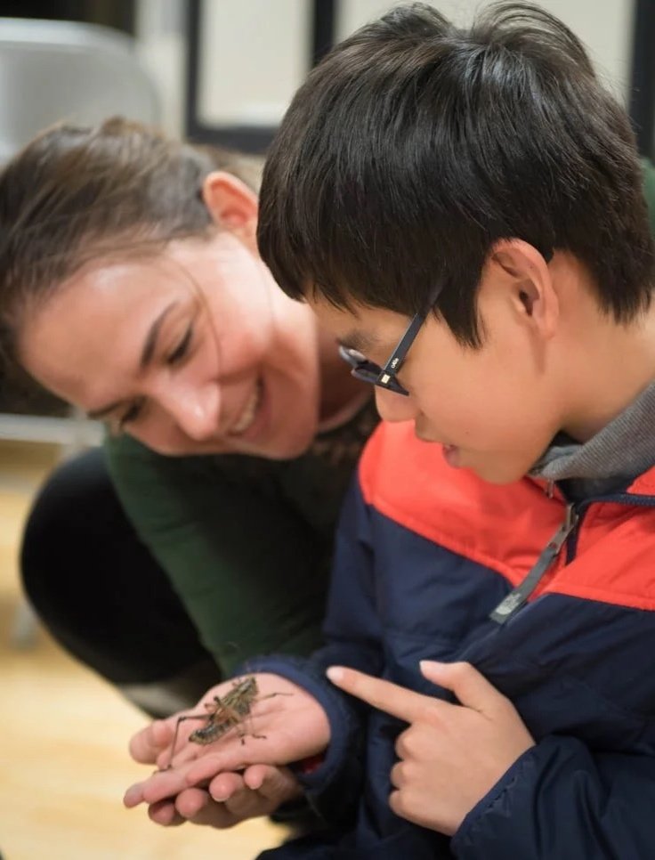A woman and a boy observe a large insect in the boy's hand.