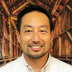 Portrait of a man smiling in front of a wooden bridge background.