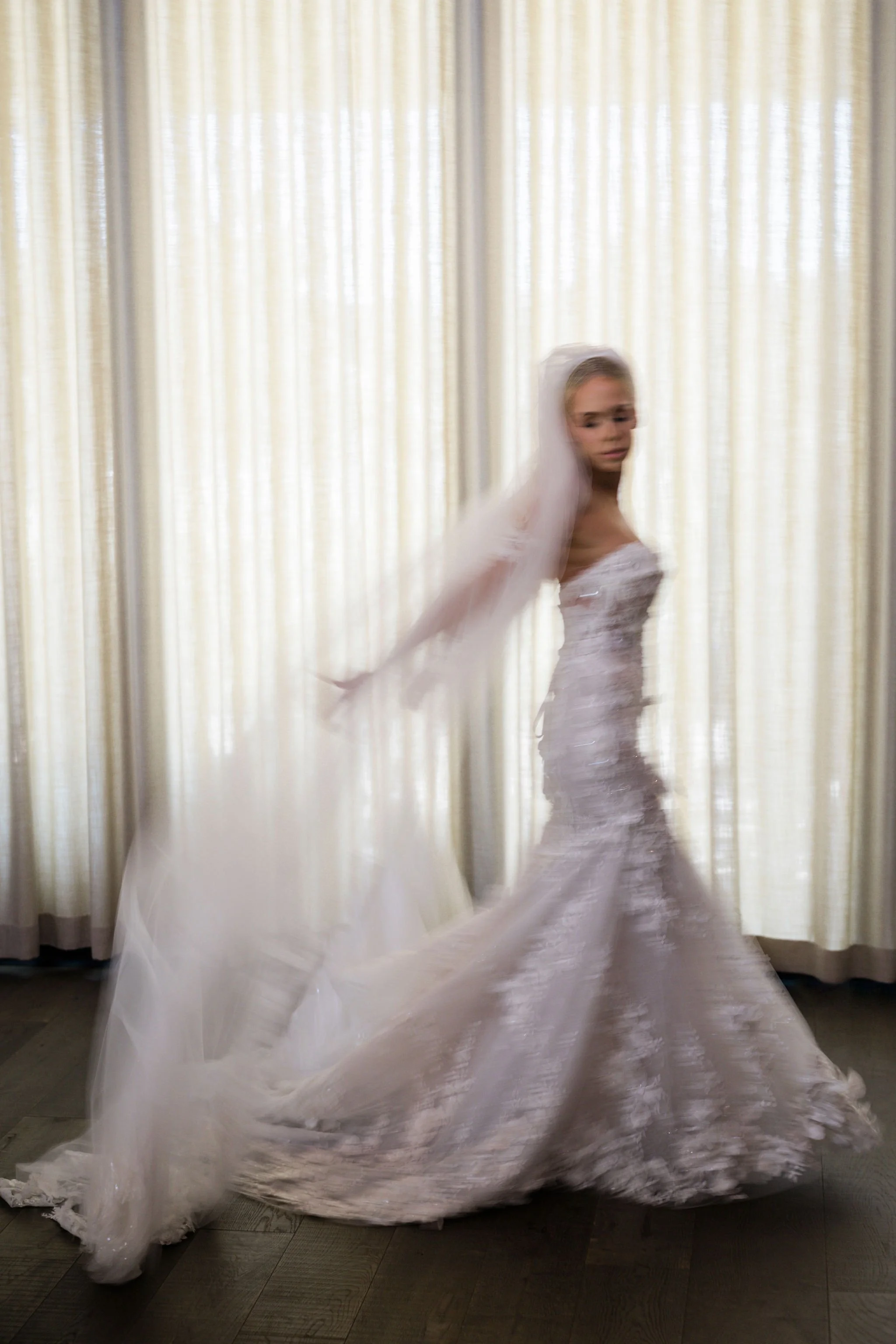 A bride in a white wedding gown twirling in front of cream-colored curtains.