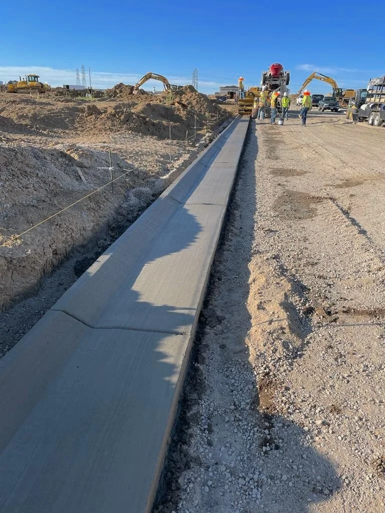 Delta Concrete Services | Construction site with freshly poured concrete sidewalk, workers in safety gear, and construction equipment.