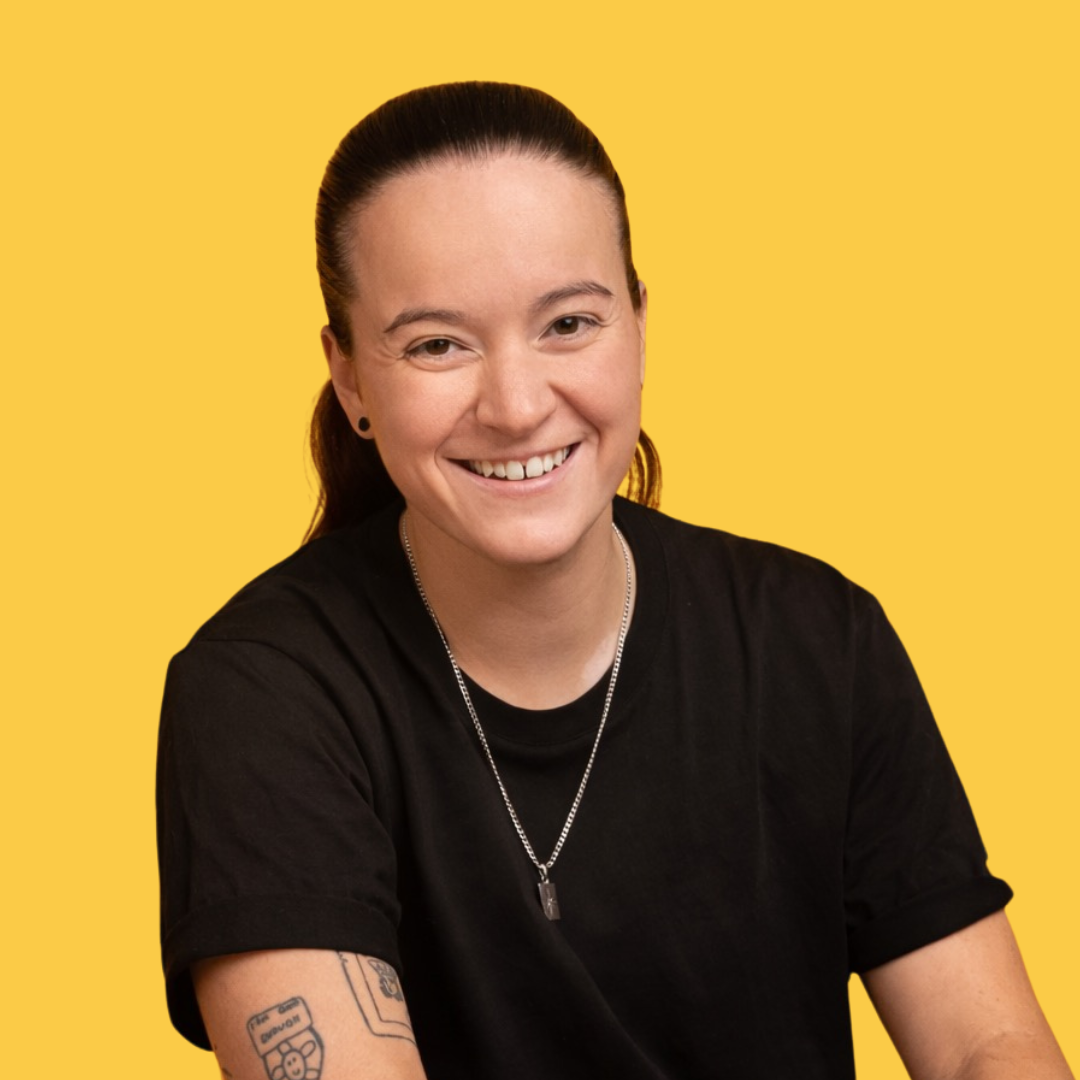 Jeune femme souriante avec tatouages, portant un t-shirt noir, fond jaune
