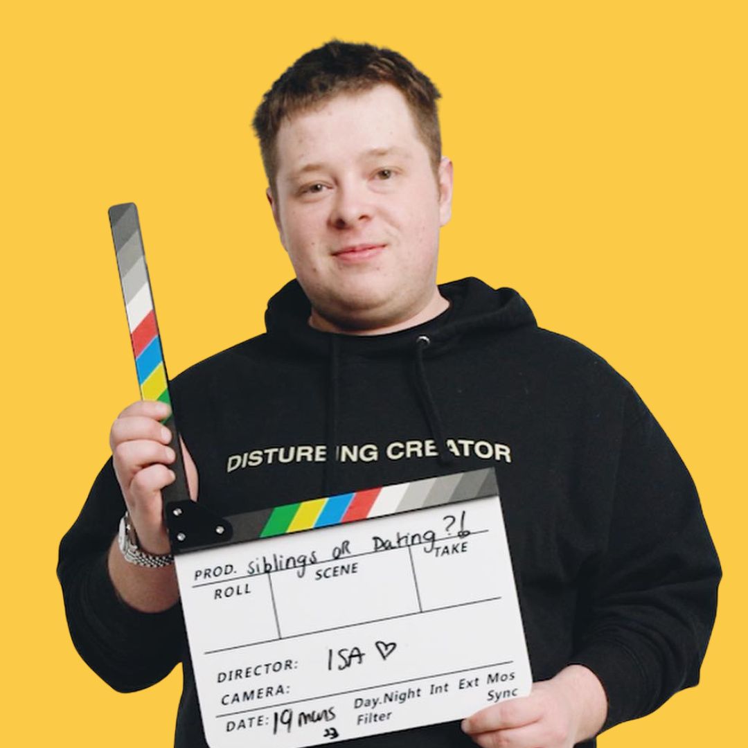 Un jeune homme tenant une claquette de tournage devant un fond jaune. Il porte un sweat noir avec écrit « DISTURBING CREATOR » et tient une pancarte indiquant un projet intitulé « siblings or dating ?! » avec la date 19 mars.