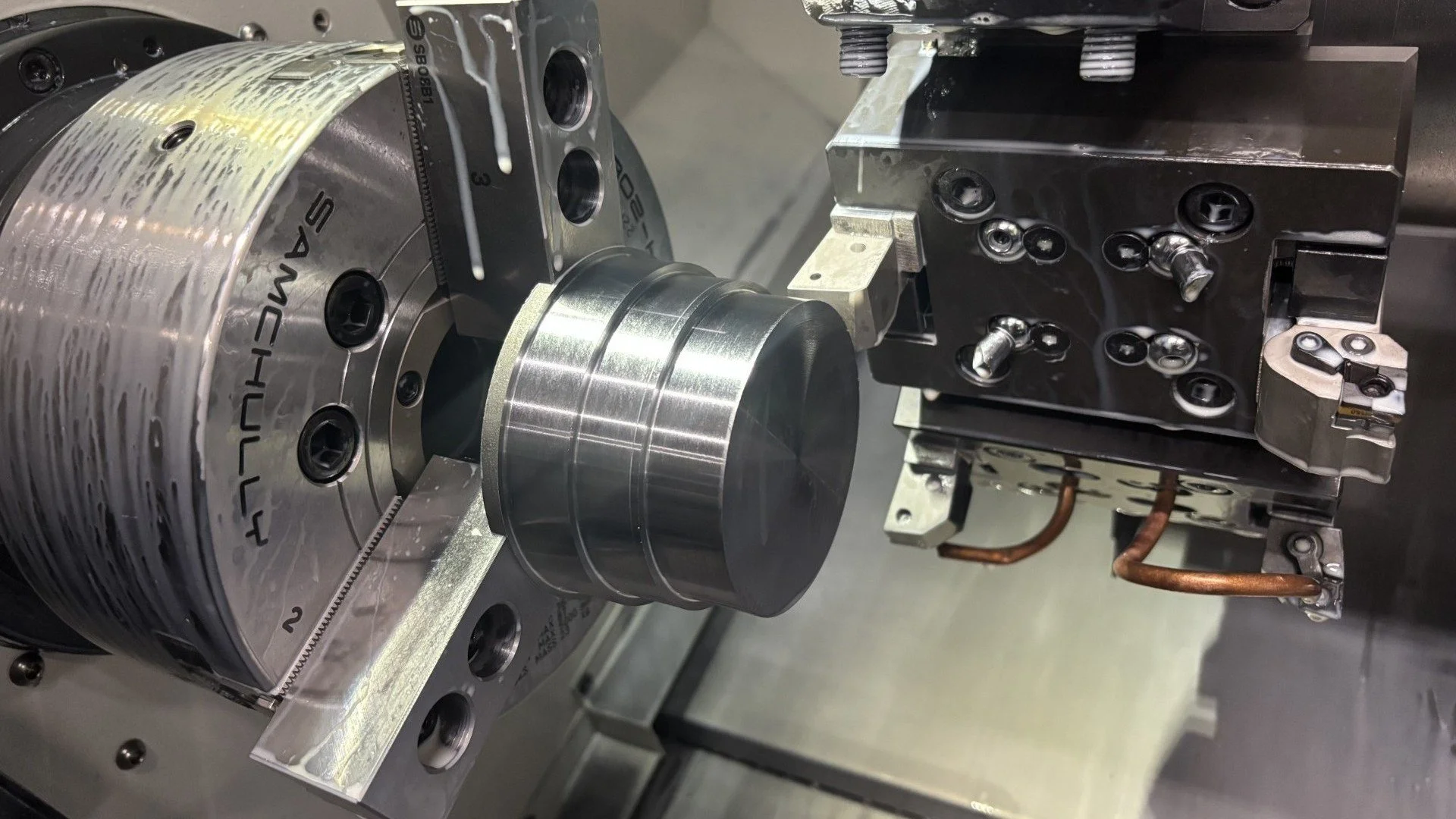 Close-up of a mechanical assembly with a large cylindrical component attached to a metal frame, featuring precise machining and multiple screws and connectors.