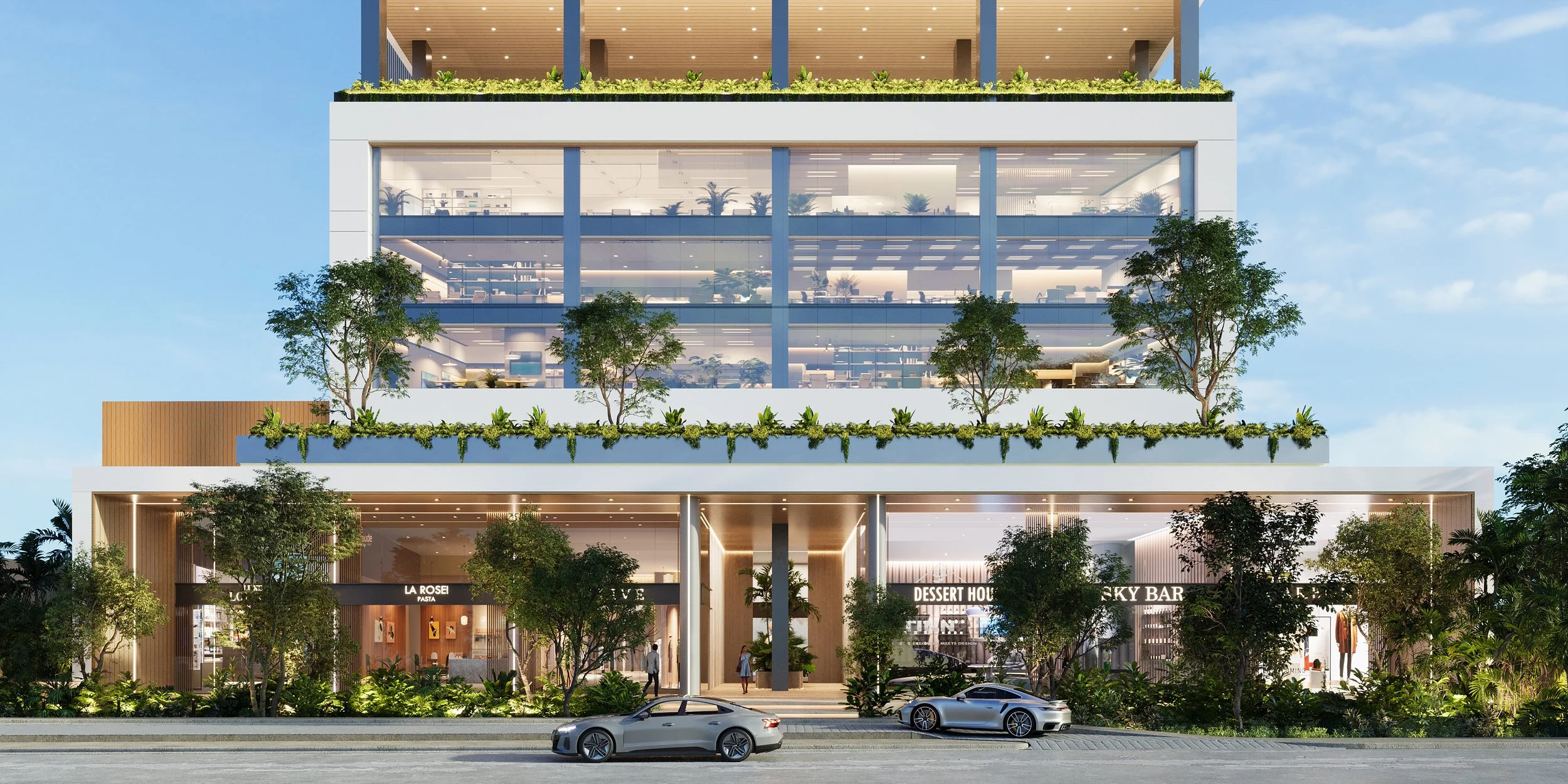Vista frontal de un edificio moderno de varios pisos con áreas verdes y árboles en cada nivel, locales comerciales en la planta baja y oficinas en los pisos superiores, con autos estacionados frente.