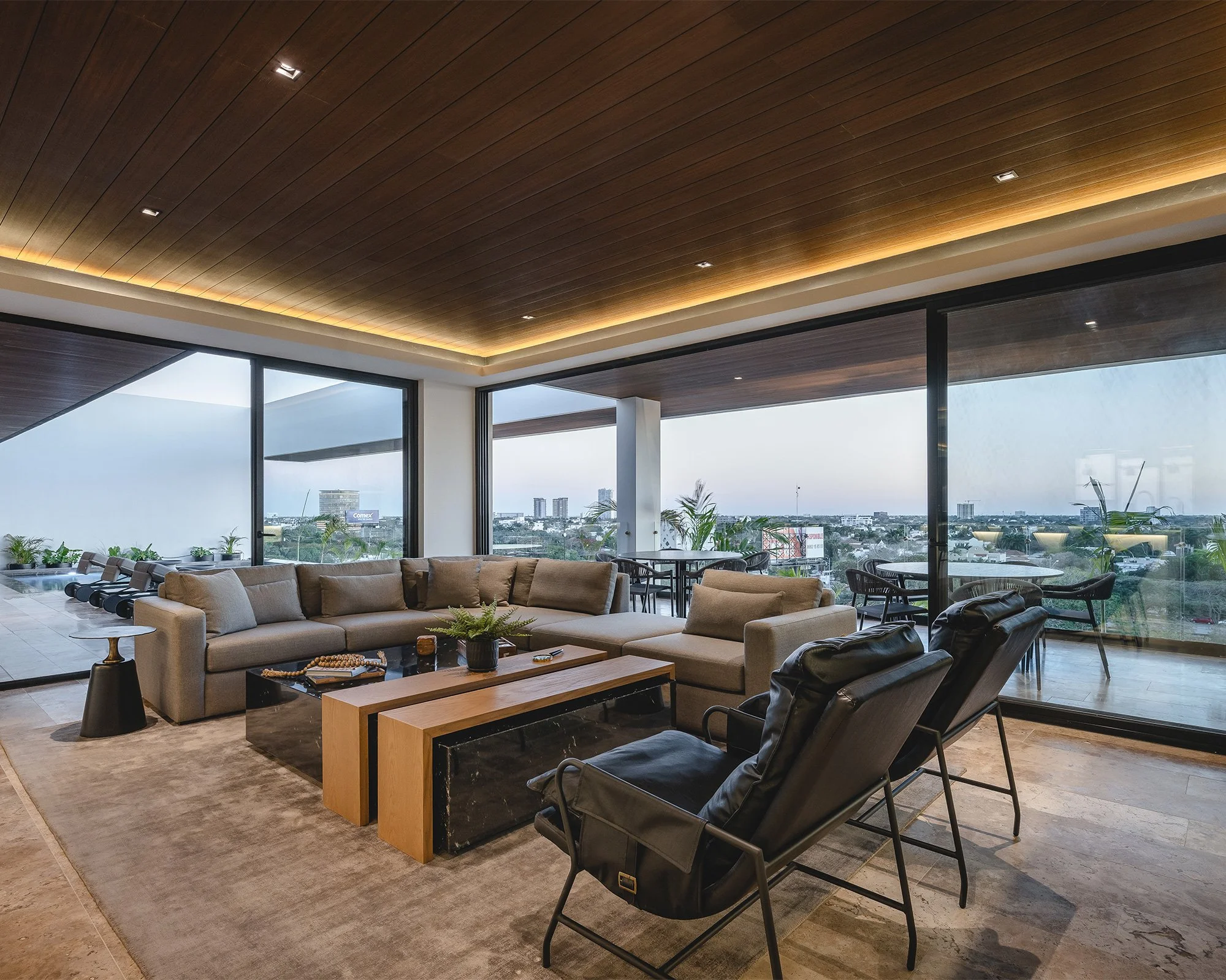 Elegante sala de estar en un edificio alto con vista a la ciudad, con sillones de color beige, sillas negras, mesas de madera, muchas plantas, y un techo de madera con iluminación empotrada, grandes ventanales y una vista panorámica del horizonte urb