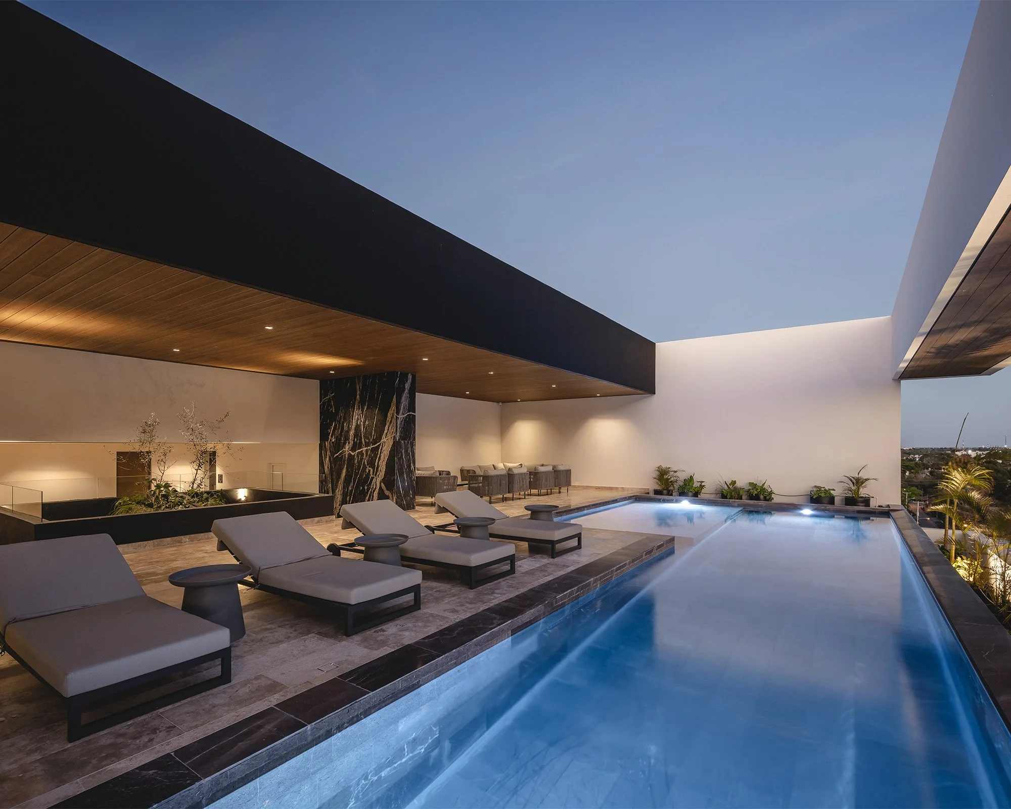Piscina iluminada de noche en un área de descanso con tumbonas y sombrillas, fondo con estructura moderna y cielo despejado.