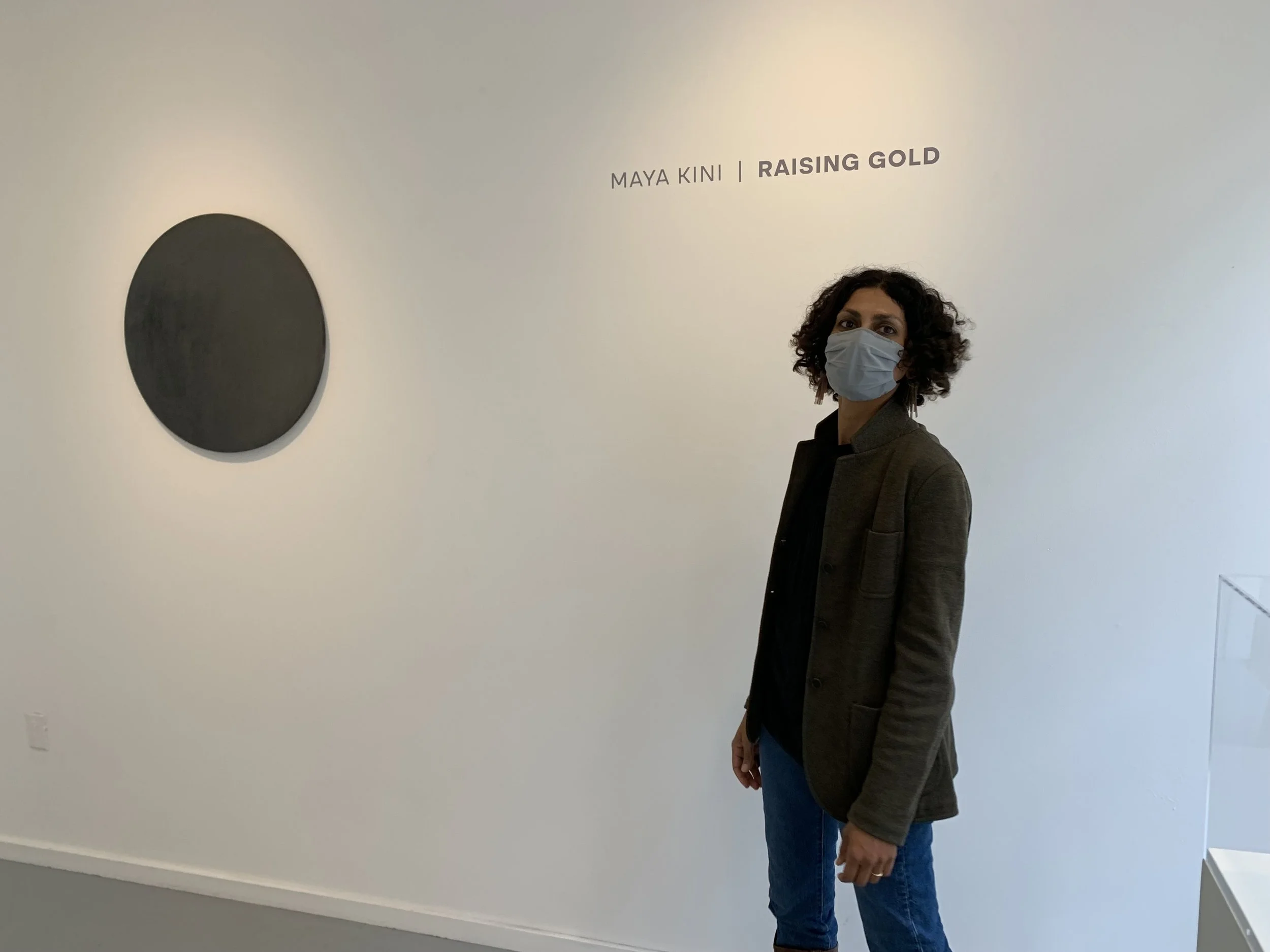 Maya standing in an art gallery at her Raising Gold opening near a black circular artwork on a white wall. 