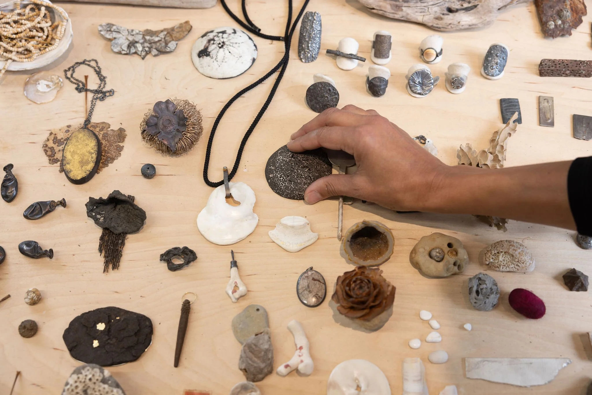 Maya's hands arranging her collection of various small rocks, shells, and artifacts on a wooden table. The items include objects from nature and the sea, beads, fossils, and decorative objects.